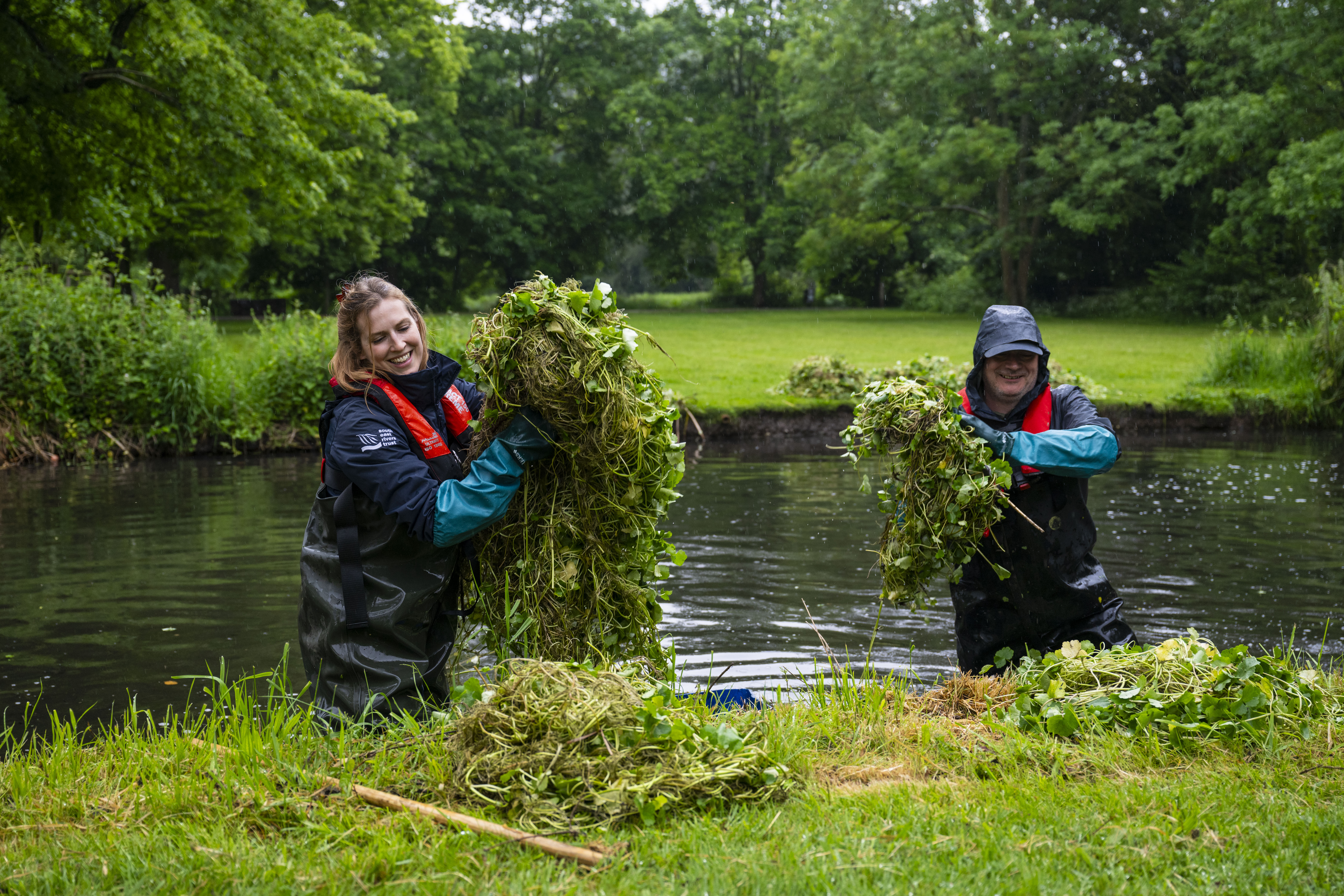 Employees from the South East Rivers Trust clearing weed from a riverbank.