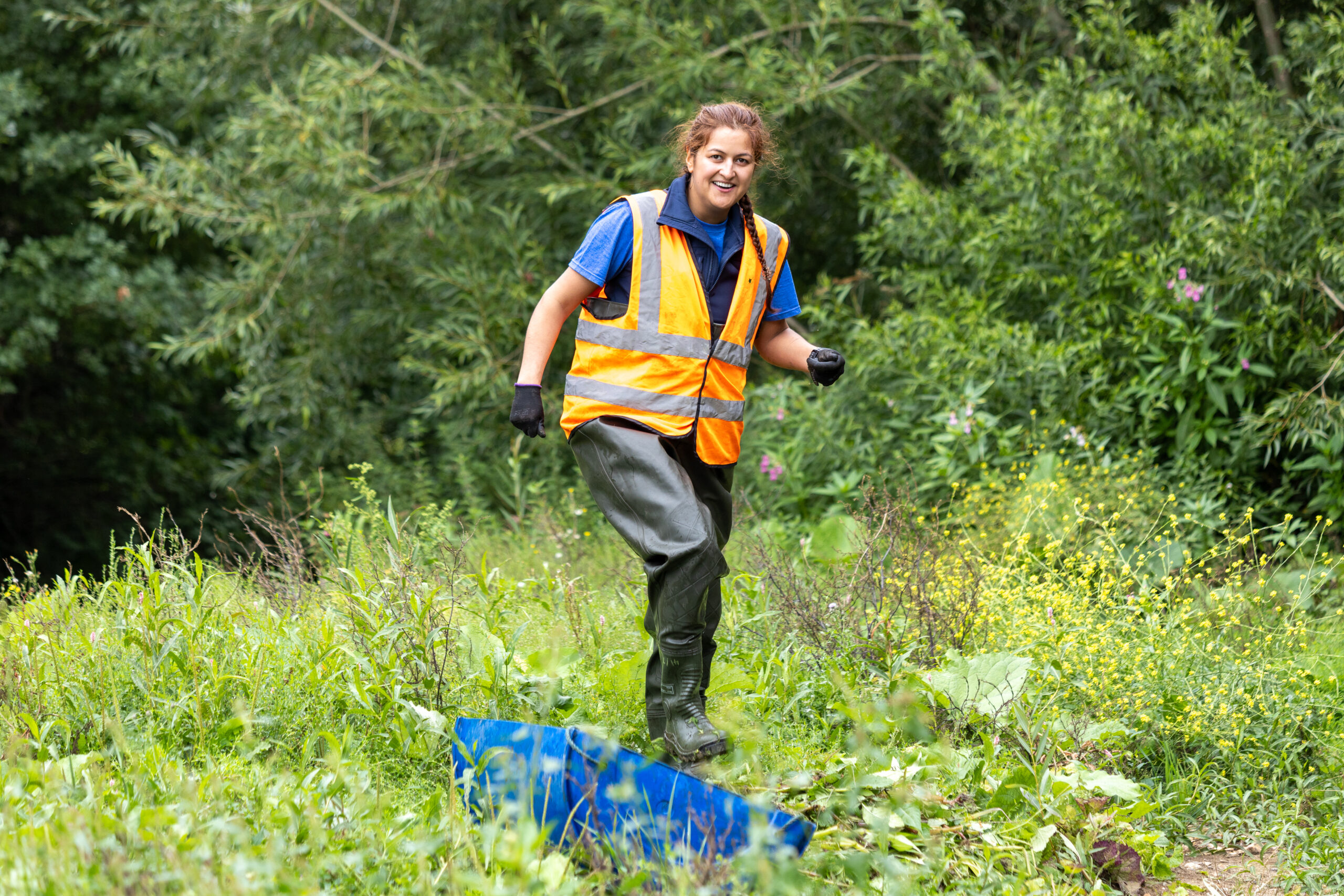 A female volunteer in a high vis vest at a river clean up event.
