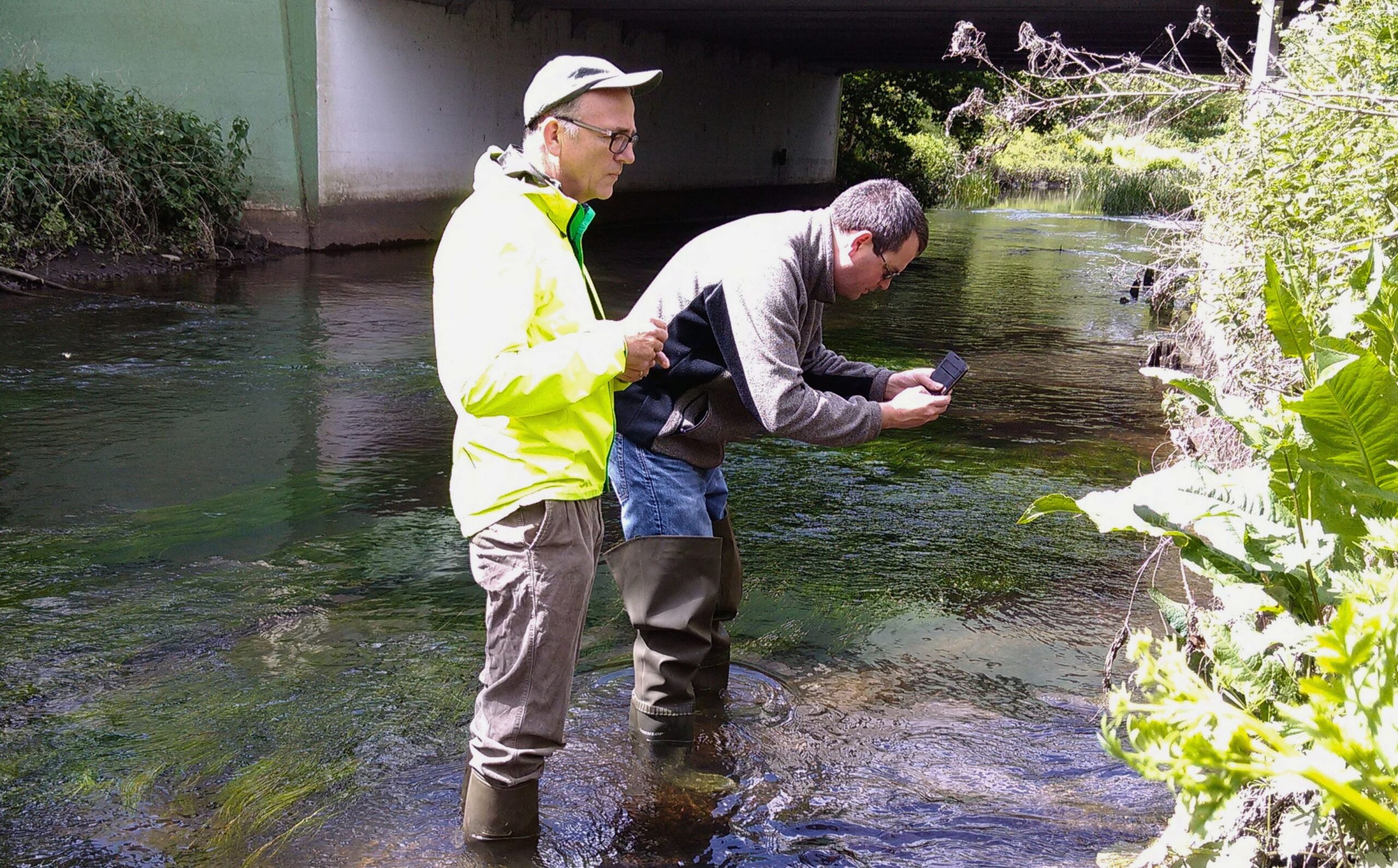 Two volunteers taking a picture of an outfall within a river.