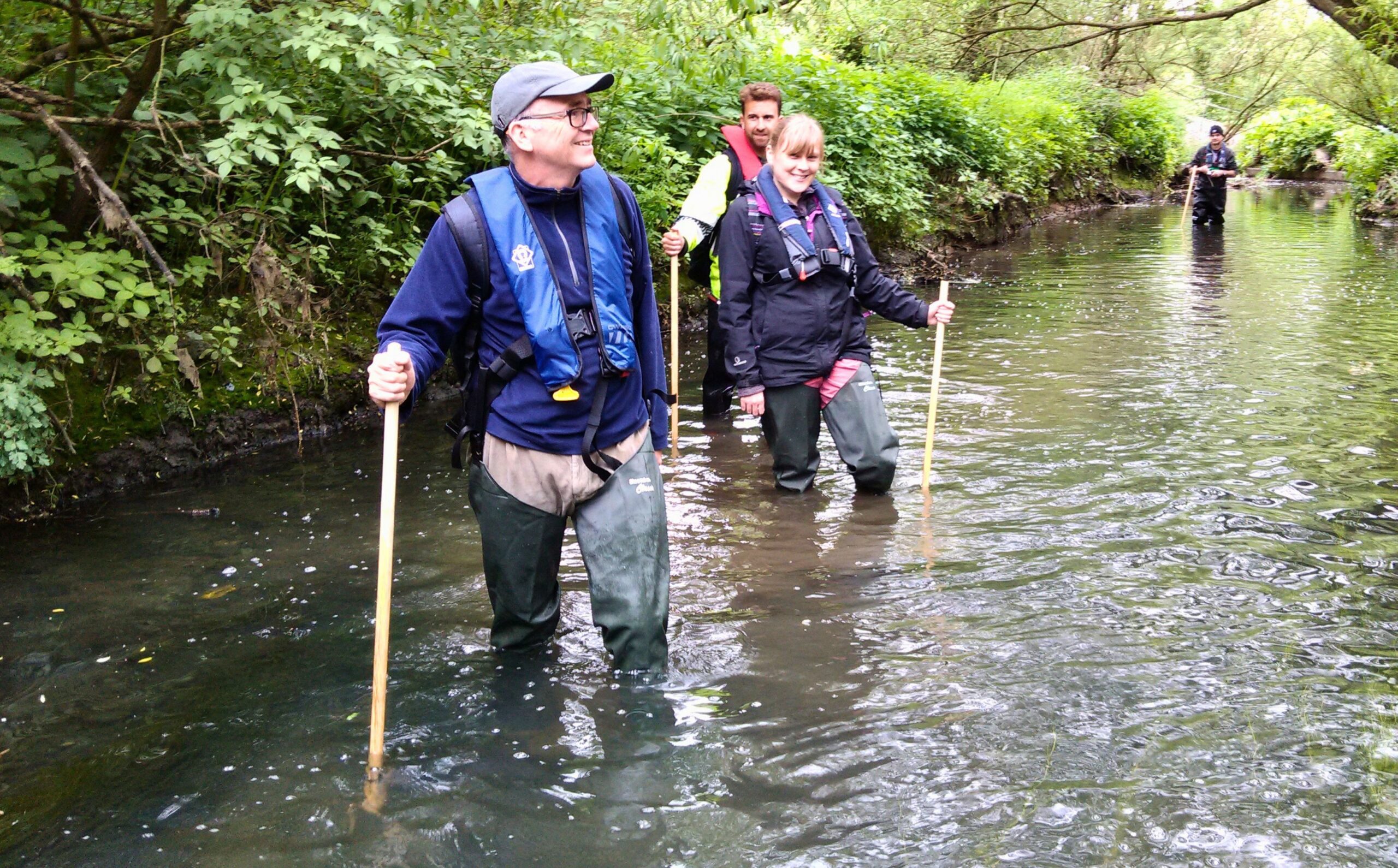 Three people standing in a river holding wooden poles during an outfall safari.