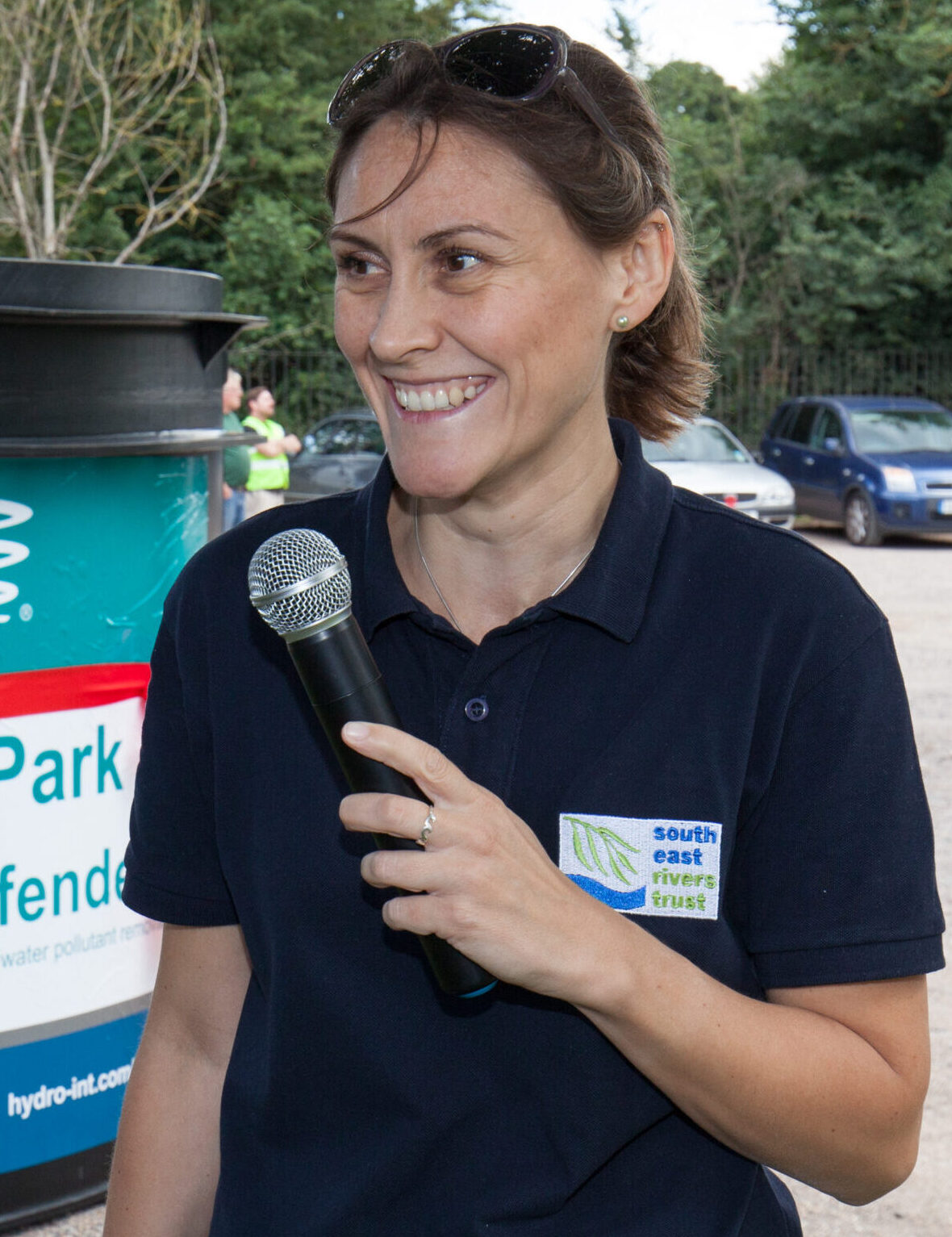 Dr Bella Davies, CEO of South East Rivers Trust, standing in front of a downstream defender with a microphone in her hand.