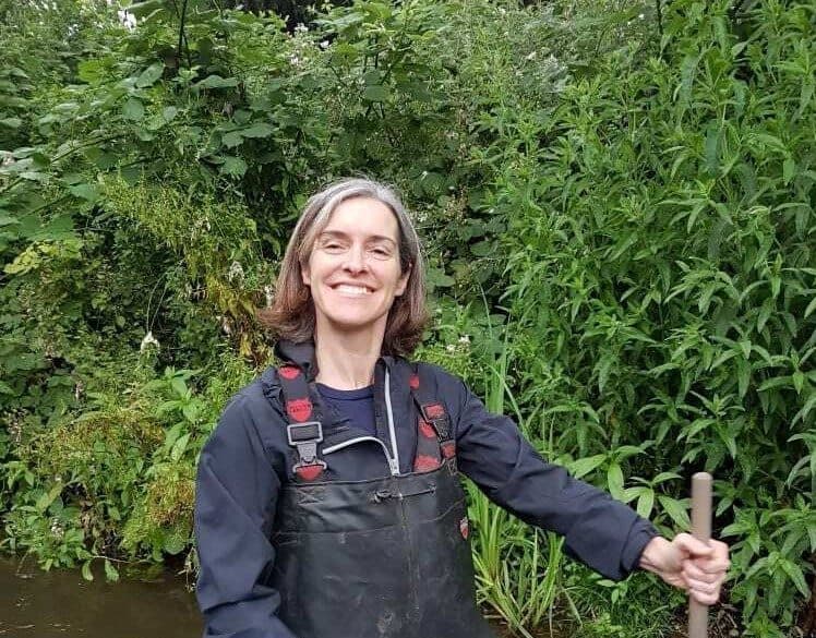 A woman, Lucy Edington, Director of Finance and Operations at the South East Rivers Trust, standing in a river with a pole in her hand.