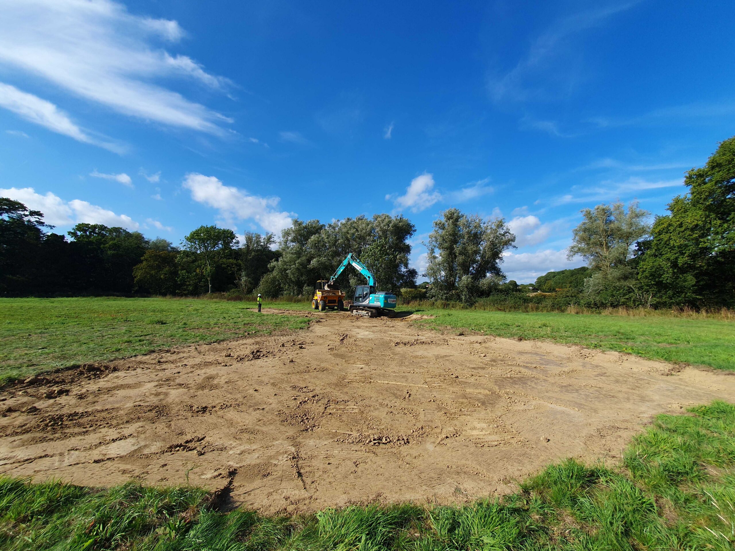 A digger behind an excavated area of a field
