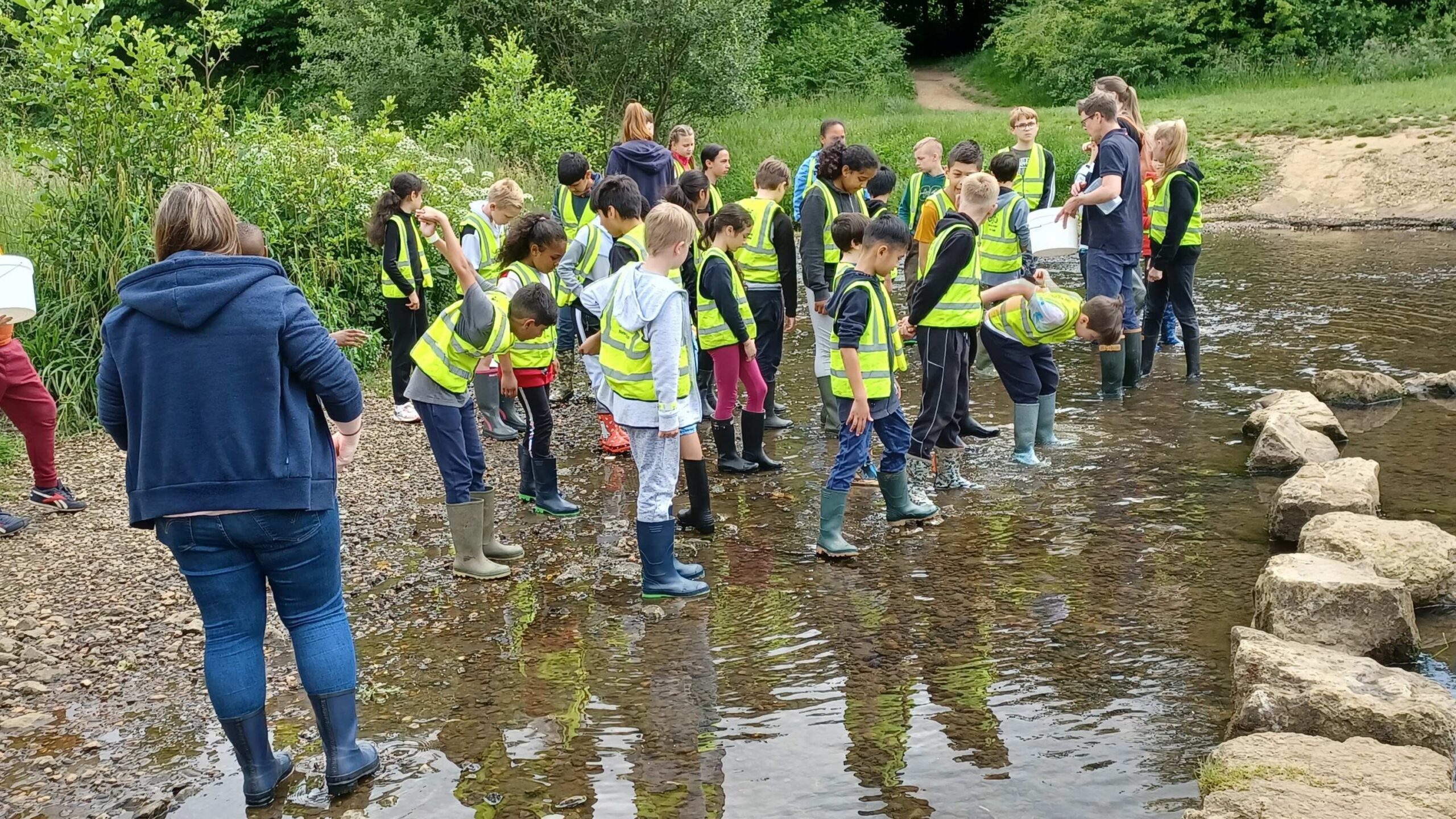 A large group of children in a shallow river getting ready for an education session