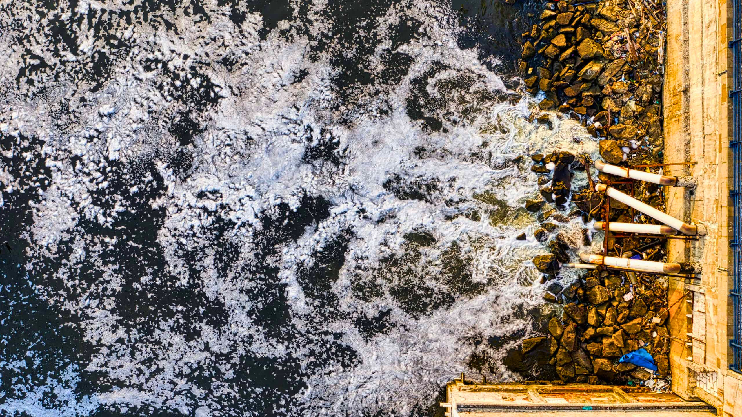 An aerial shot of pipes overflowing into the sea.