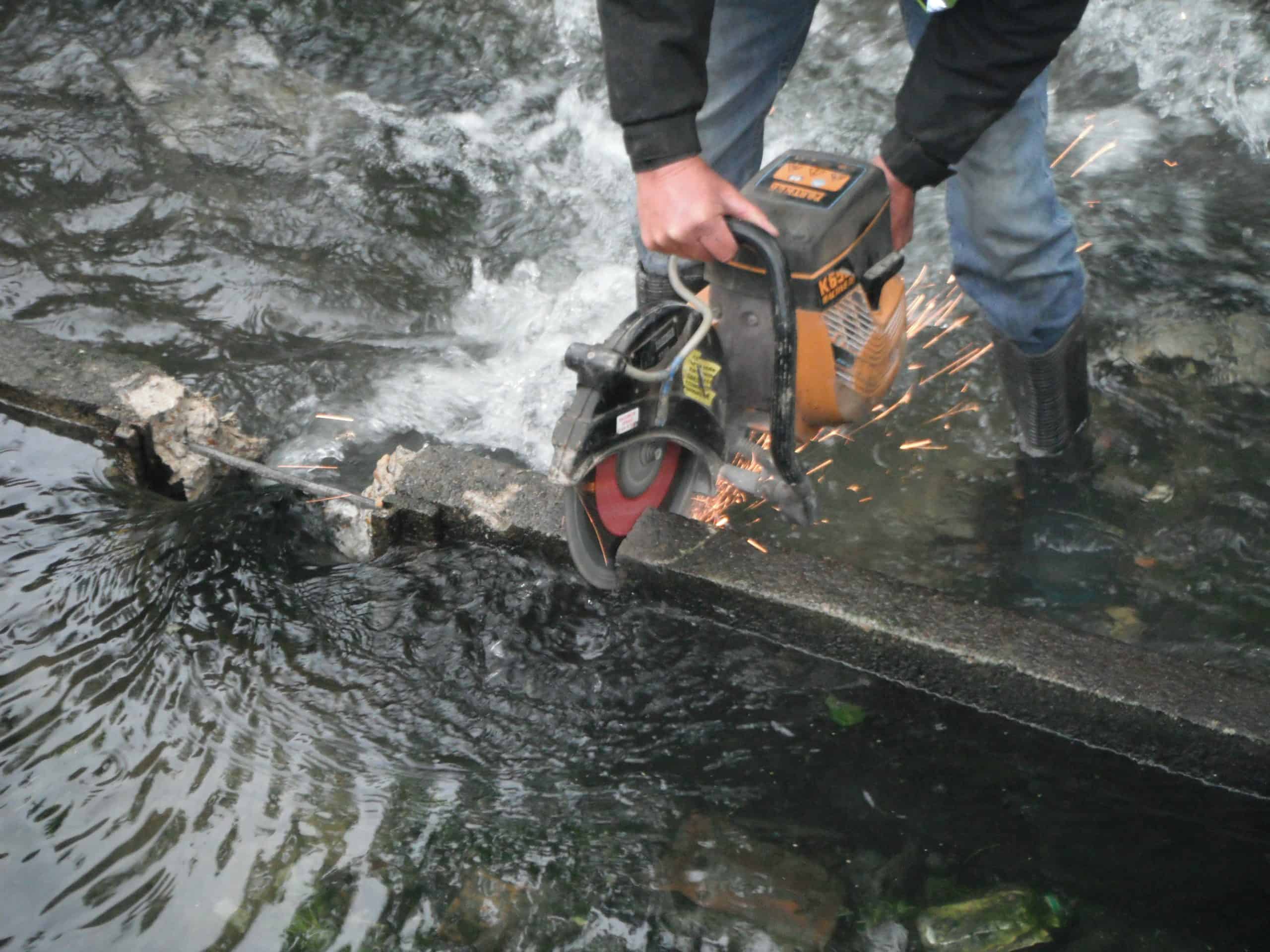 Restoration work being done using a circular saw to notch the weir to allow fish to pass the weir