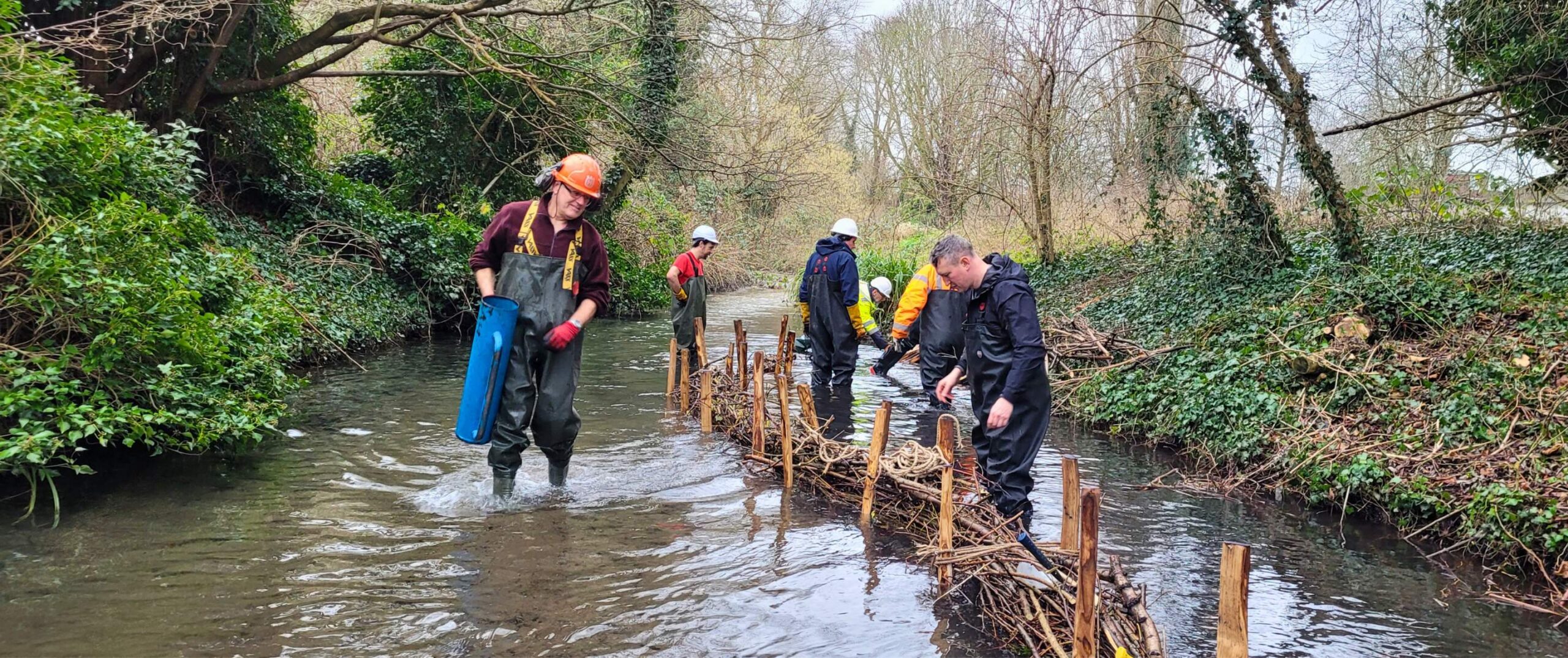 A group of 5 volunteers working together at the edge of the river creating a berm to slow the flow of the river