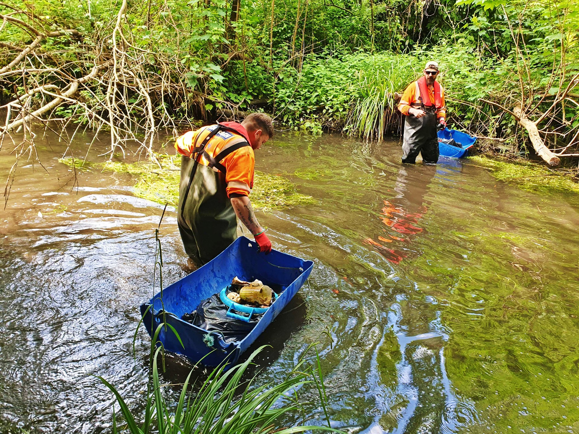 Two men in high vis vests standing in a river collecting litter.