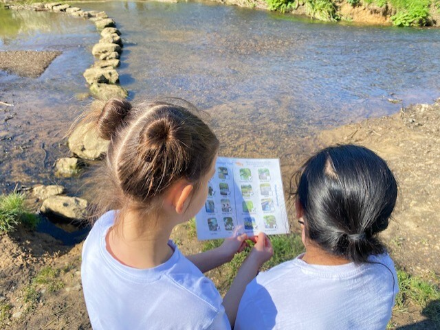 Two girls standing in front of a river looking at a sheet of paper.