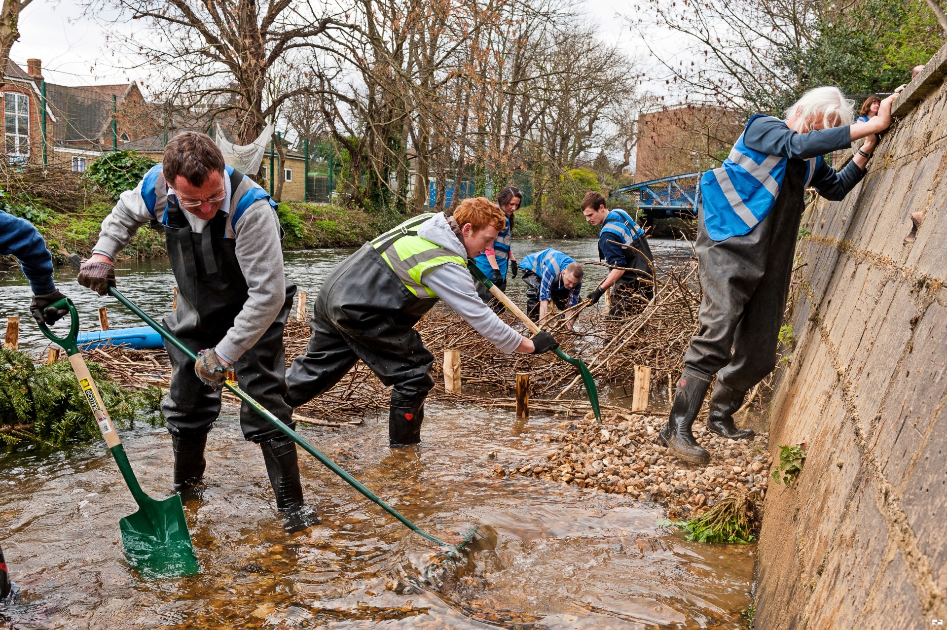A group of people wearing waders and using tools in a river.