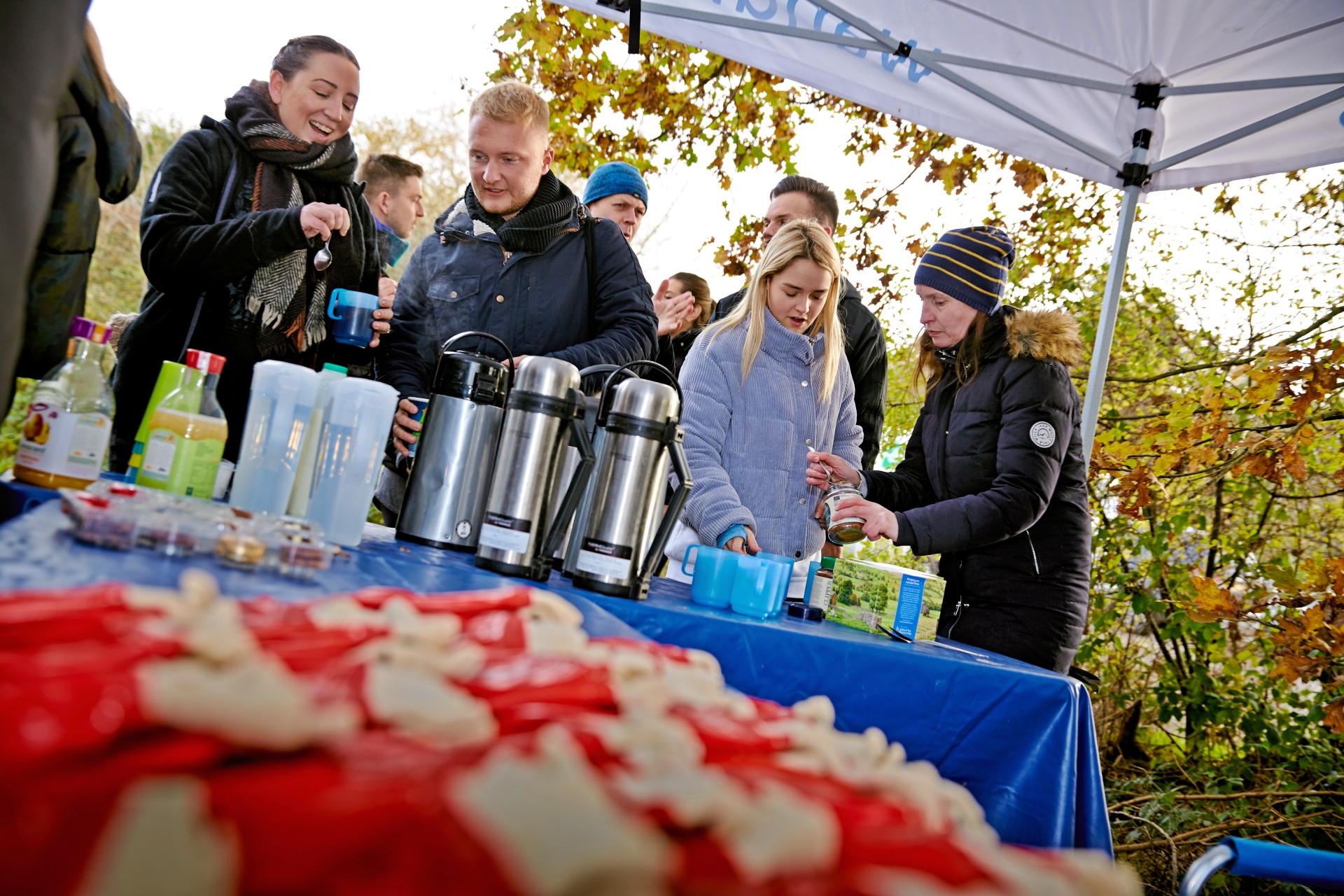 A group of people standing under a gazebo and preparing hot drinks.