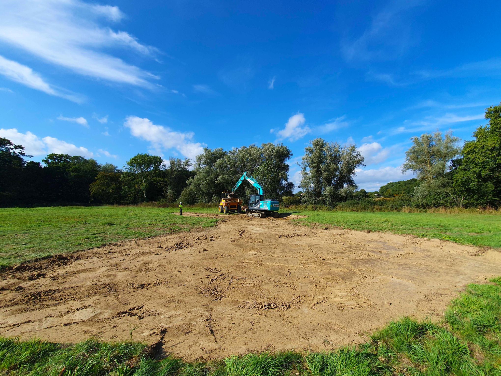 A large area of mud that has been dug in a field with a blue digger in the distance.