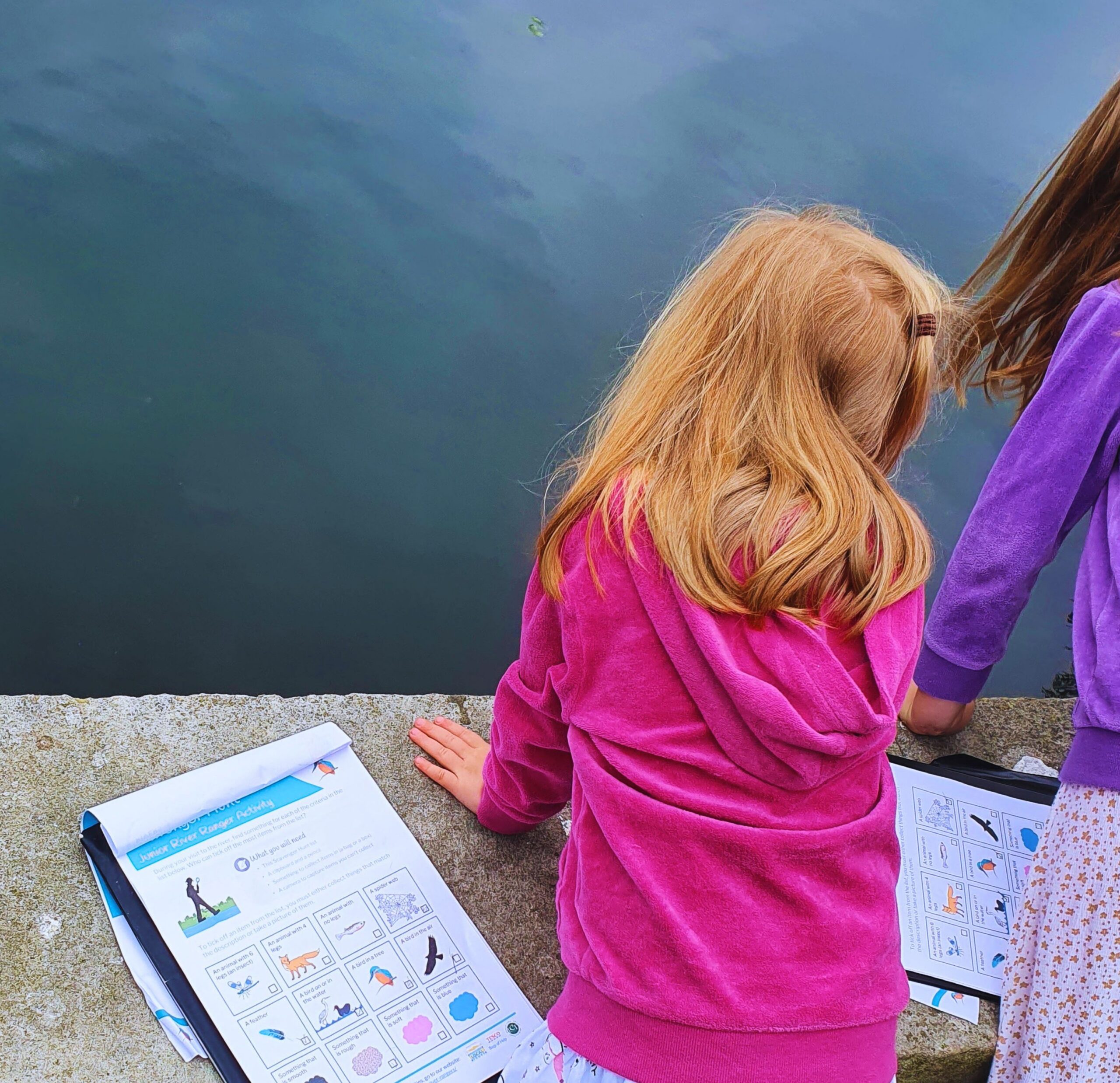 Two girls standing in front of a river with clipboards.