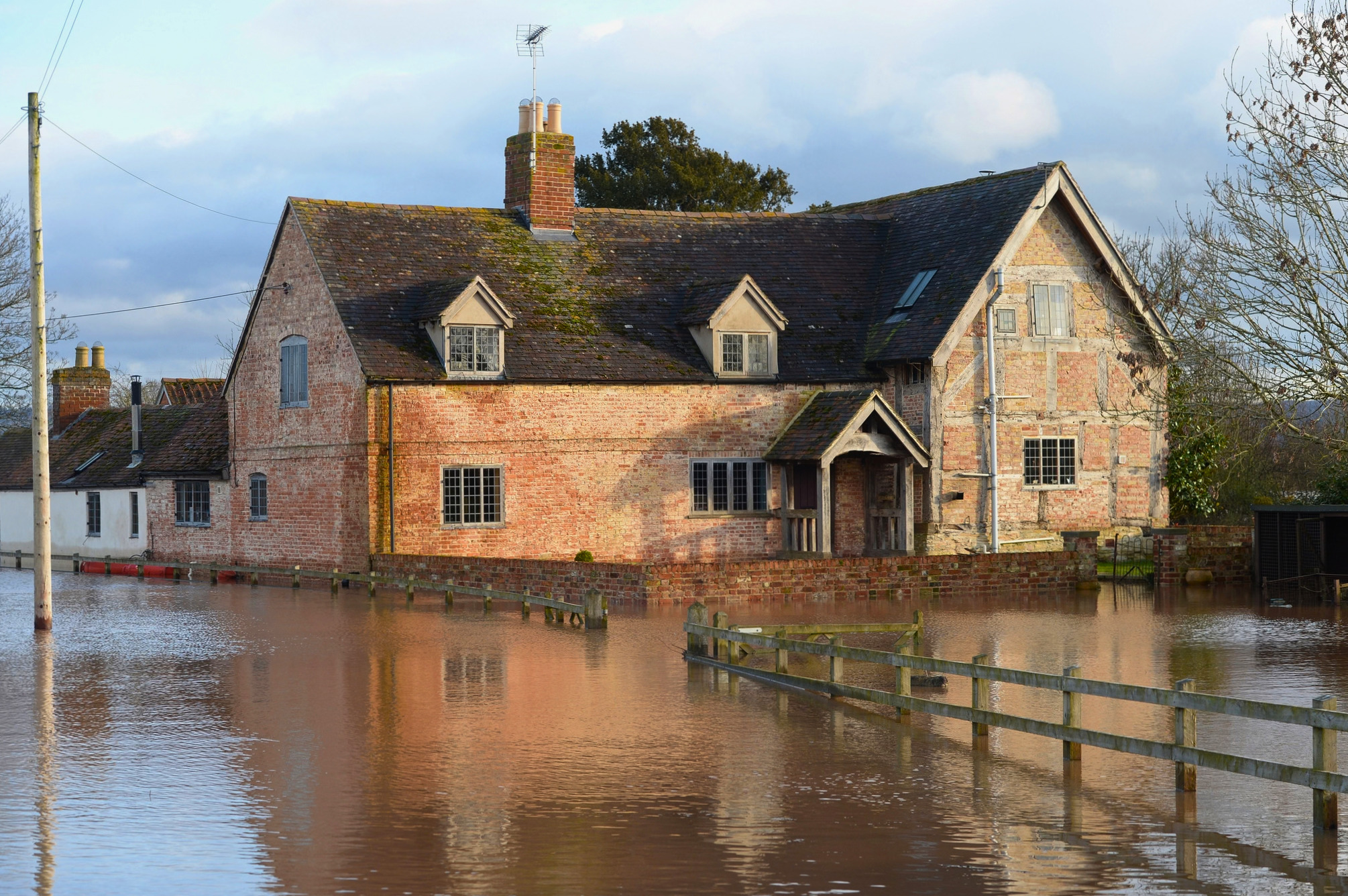 A large red brick house with beams is surrounded with flood water.